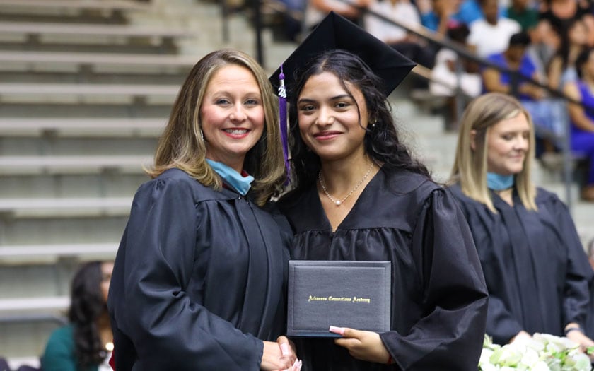 A graduate of Arkansas Connections Academy with her diploma shakes the hand of the Arkansas Connections Academy staff member.