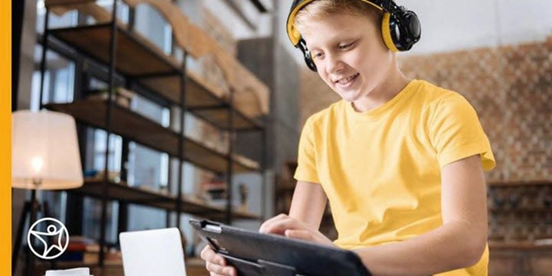A young student is wearing headphones while interacting with his tablet